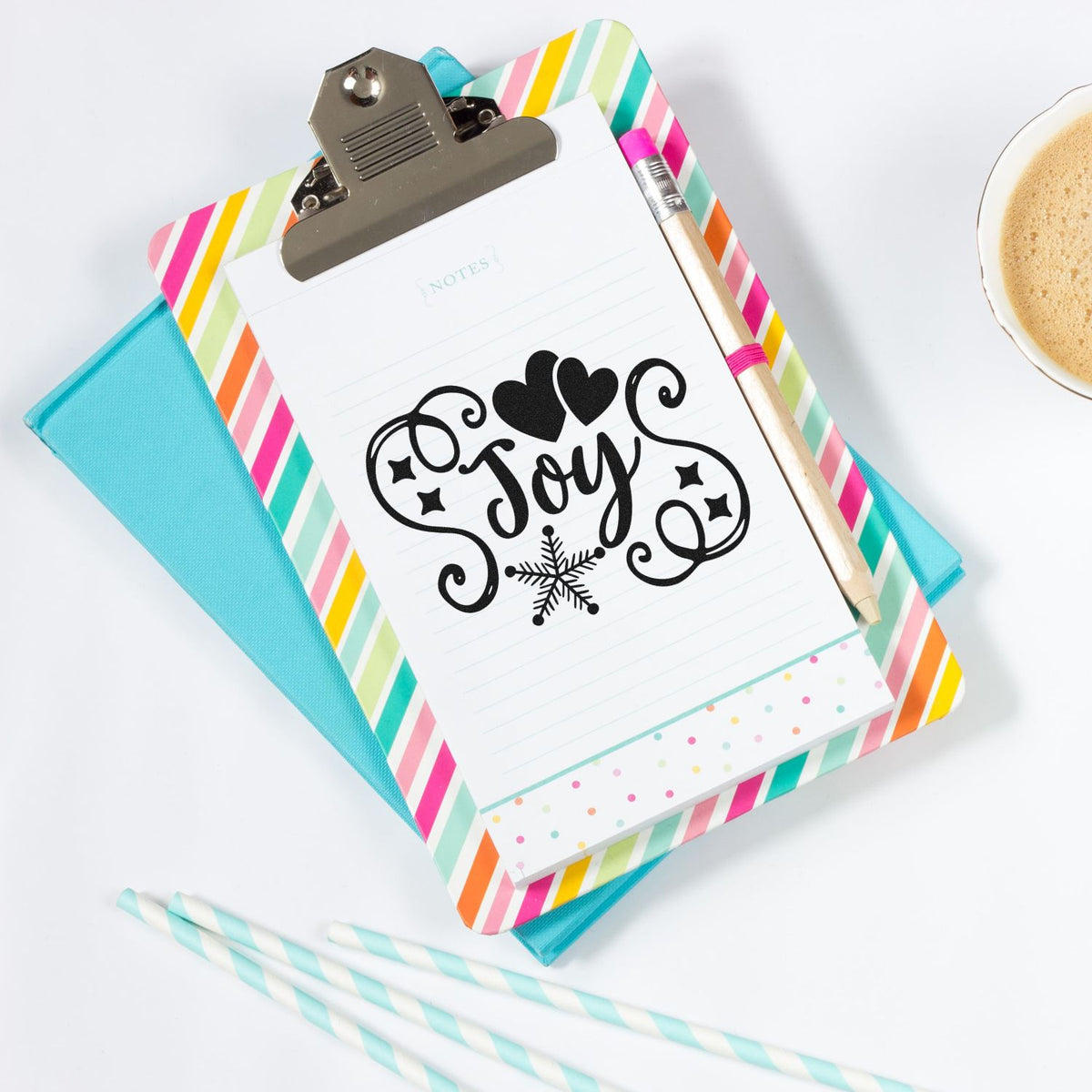 Black Joy stamp and seal design on striped clipboard, with hearts, snowflake, pastel notebook, and aqua folder.