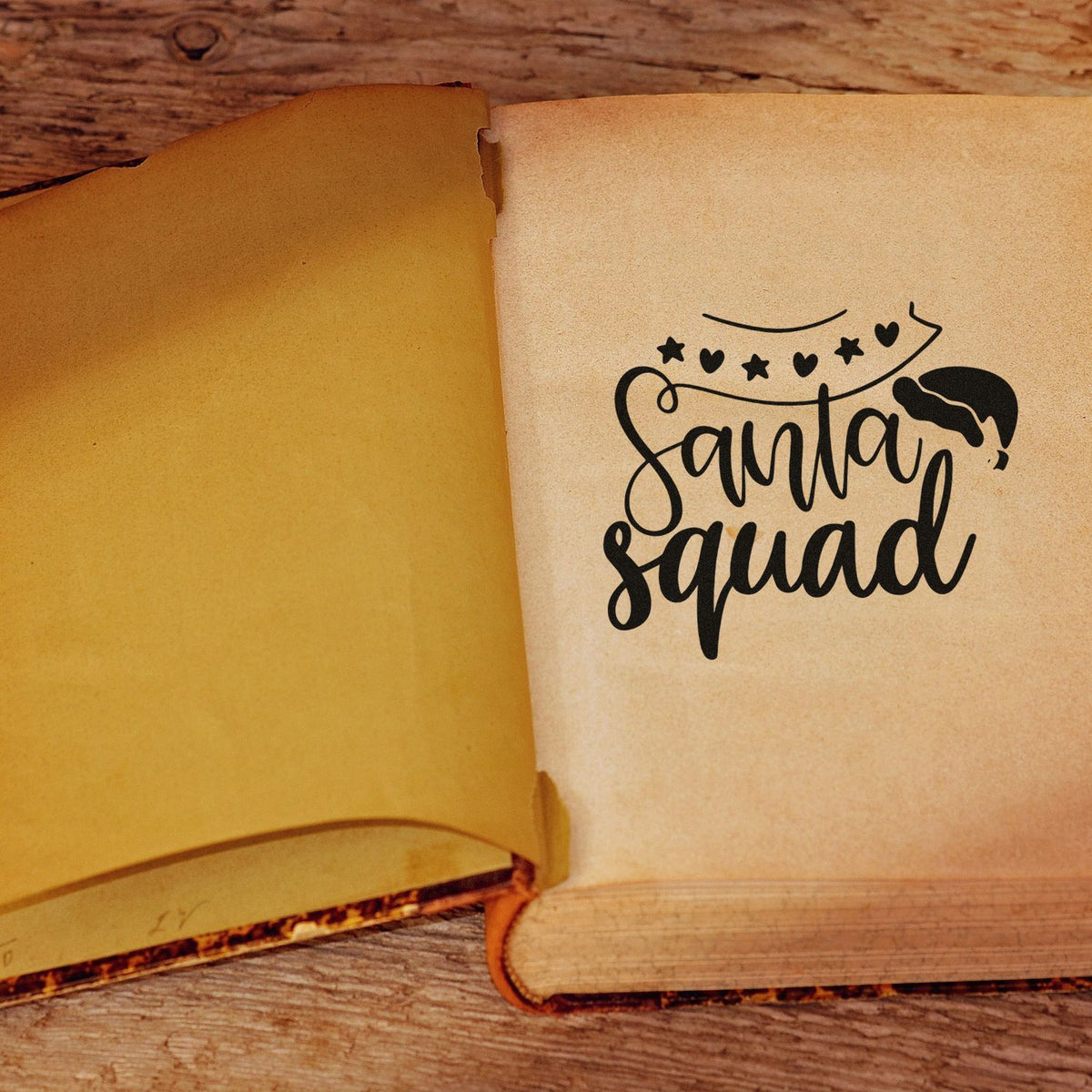 Santa Squad black stamp design with stars and hearts on cream paper, styled like a festive seal on an open book.