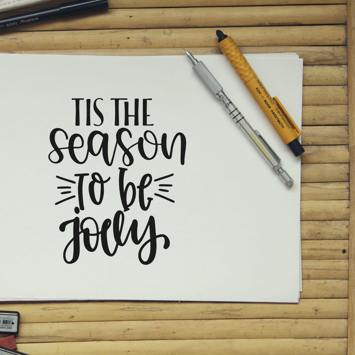 Black calligraphy quote on white paper with silver and gold stamp-and-seal tools on a bamboo desk