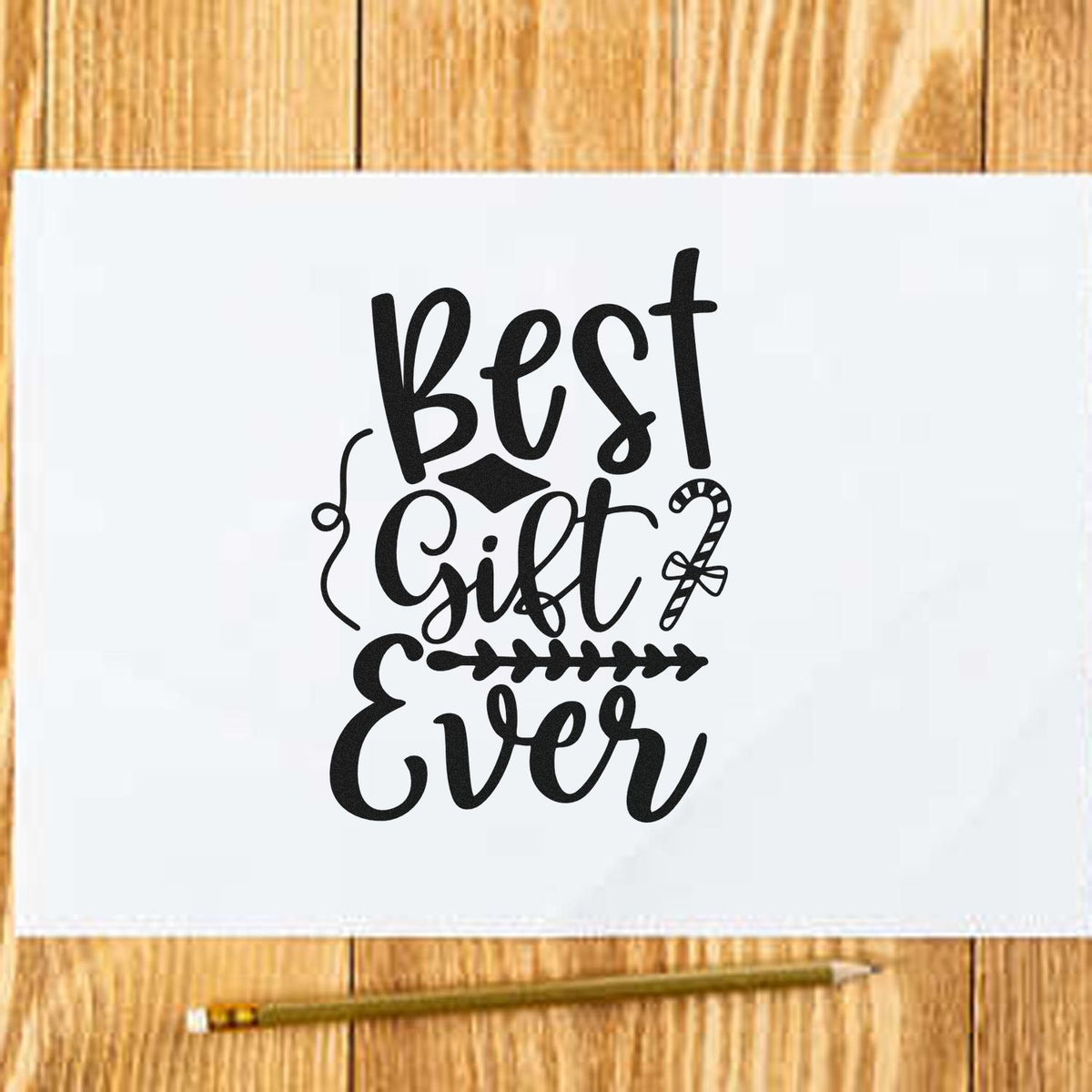 Black Best Gift Ever stamp and seal design on a white napkin, with candy cane and leaf accents on a light wood table.