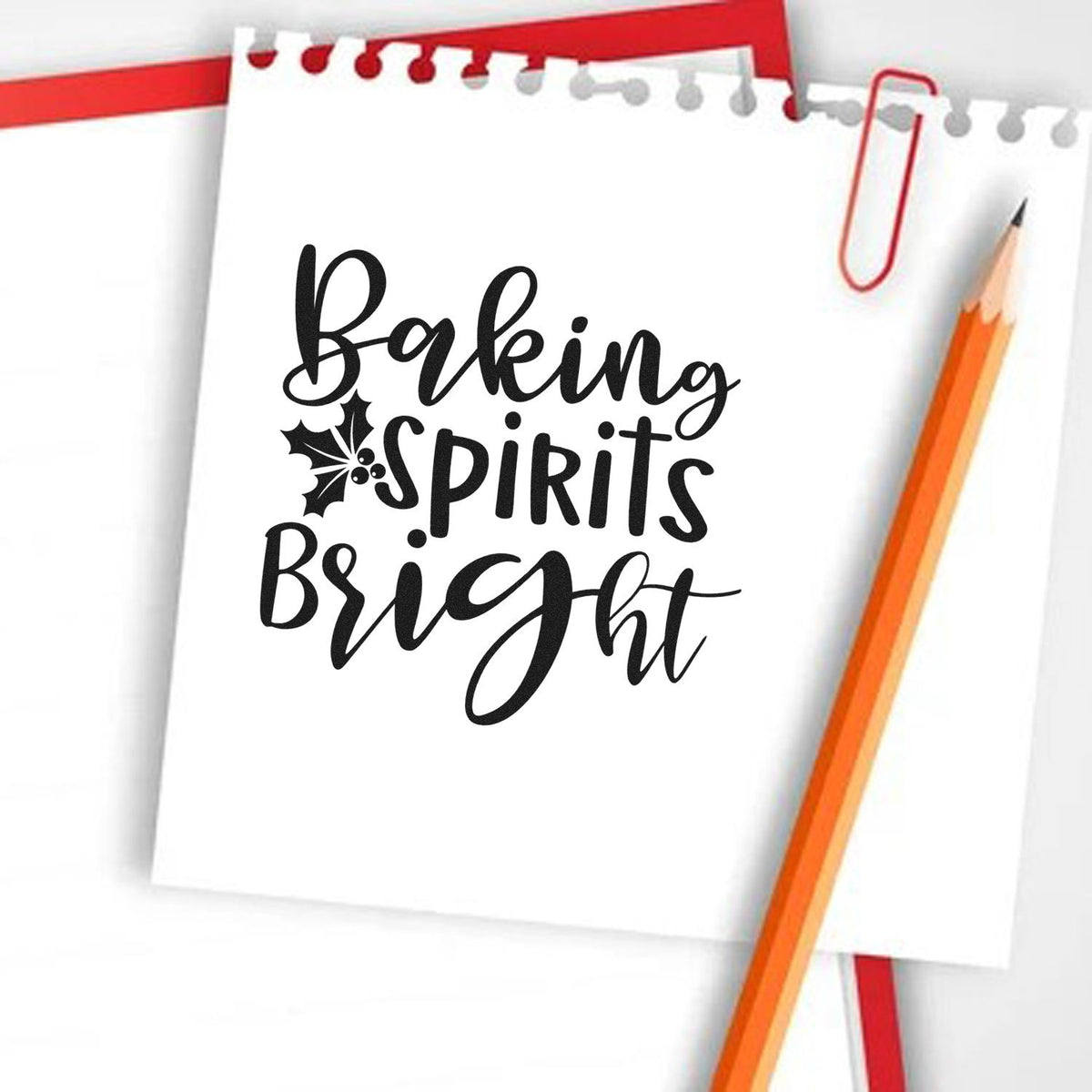 Black Baking Spirits Bright holiday stamp and seal on white paper, with holly, red paperclip, and orange pencil.