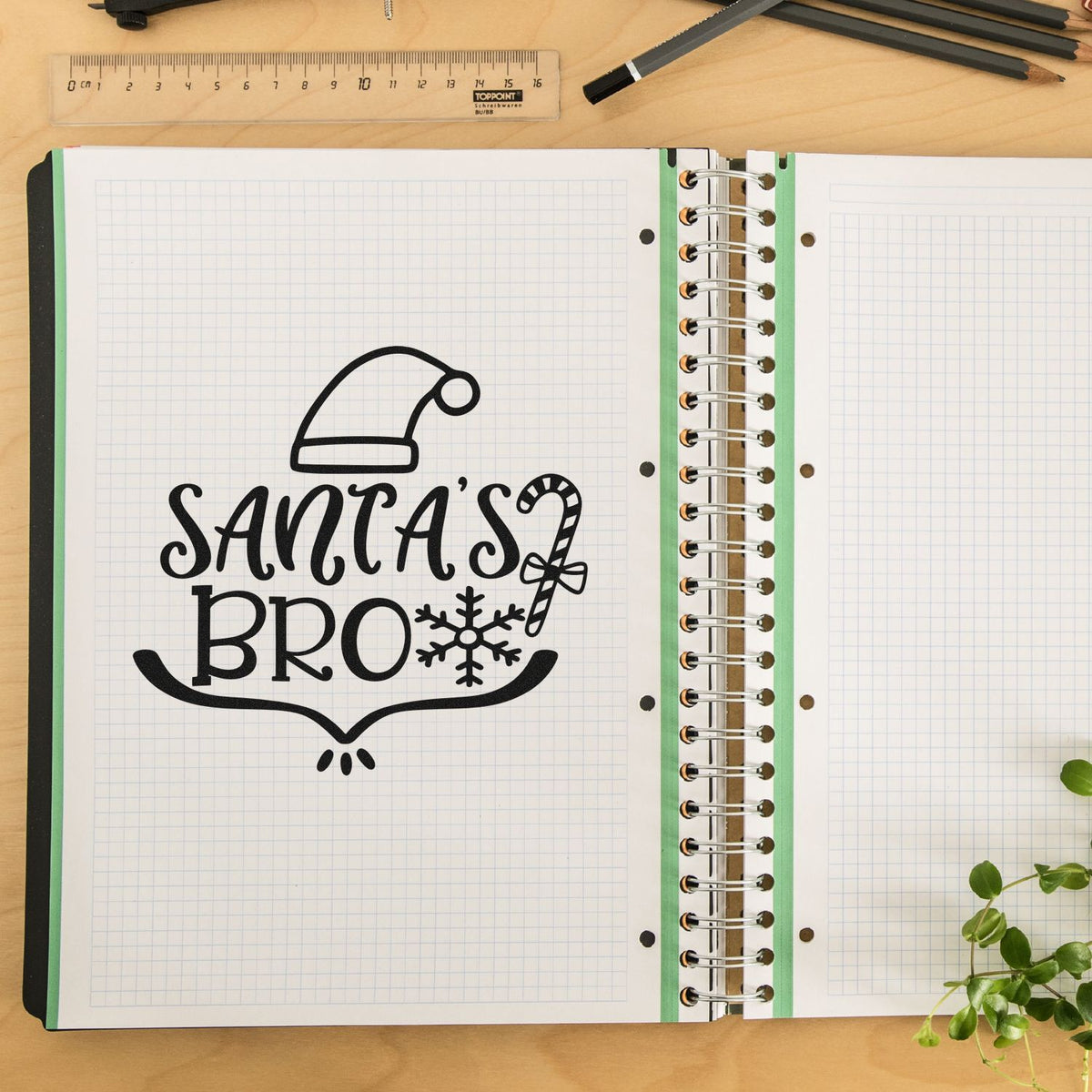 Black holiday stamp seal reading Santas Bro on white grid notebook pages, with Santa hat, candy cane and snowflake.