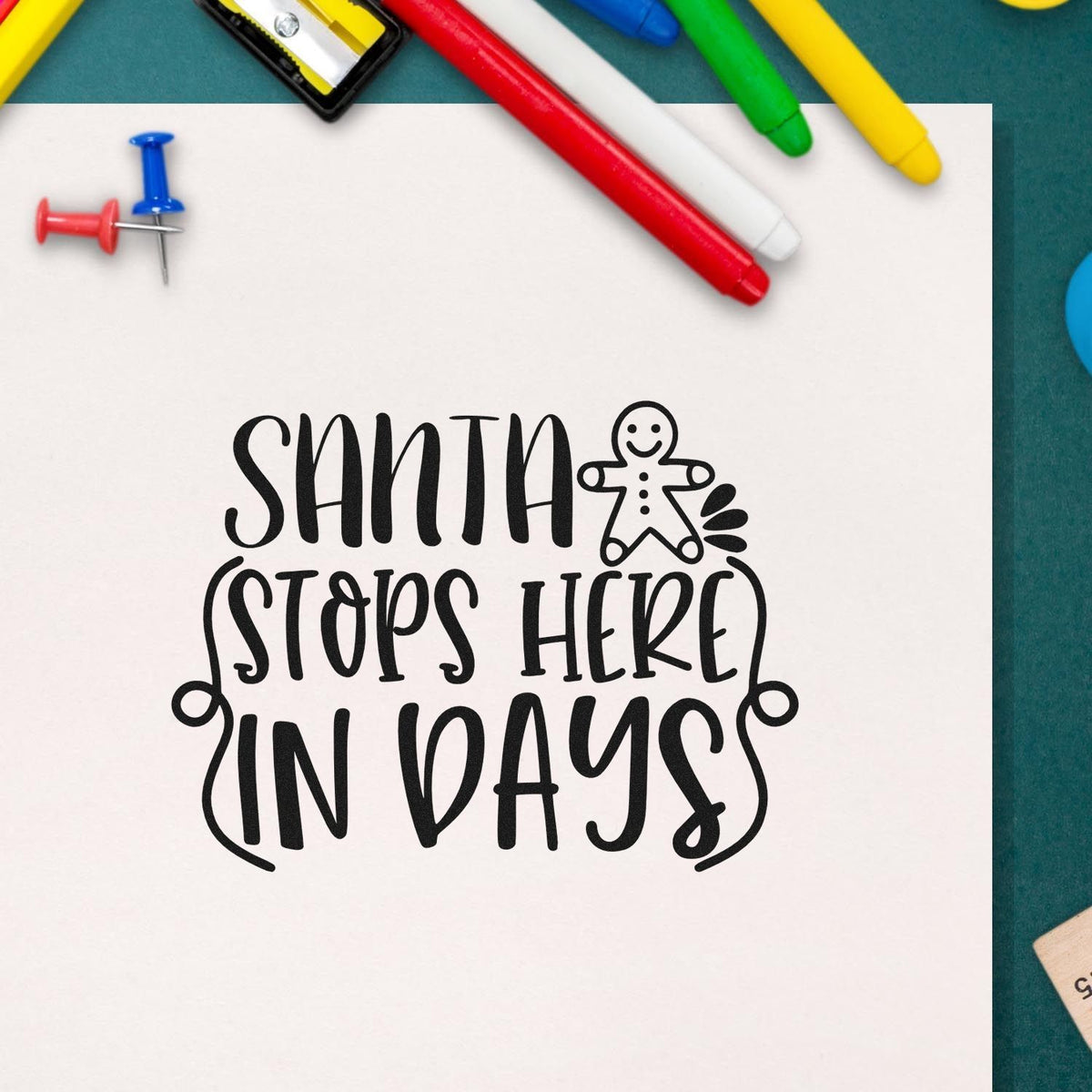 Black Santa Stops Here in Days stamp design with gingerbread figure, on white paper beside red, blue, green, and yellow markers.