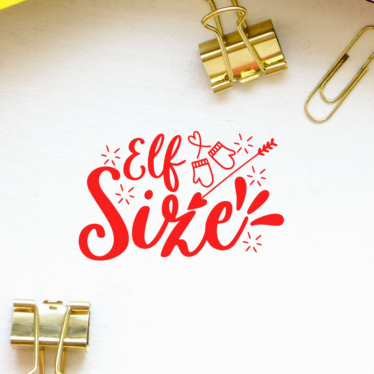 Red Elf Size! stamp/seal design with mitten-and-arrow graphic, clipped on white paper with gold binder clips.