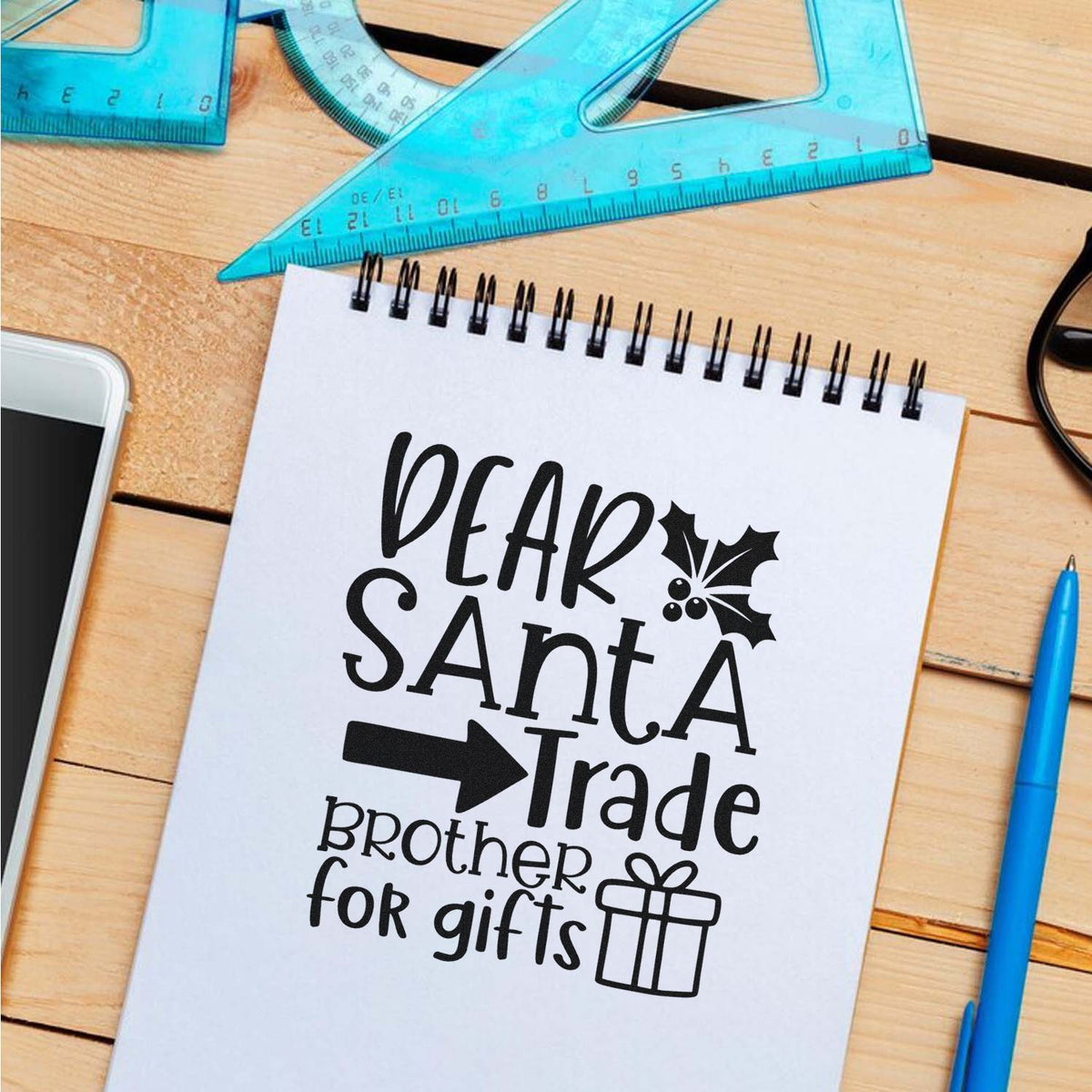 Black holiday stamp and seal design on a white notebook, reading Dear Santa Trade Brother for gifts, with holly and gift icon.
