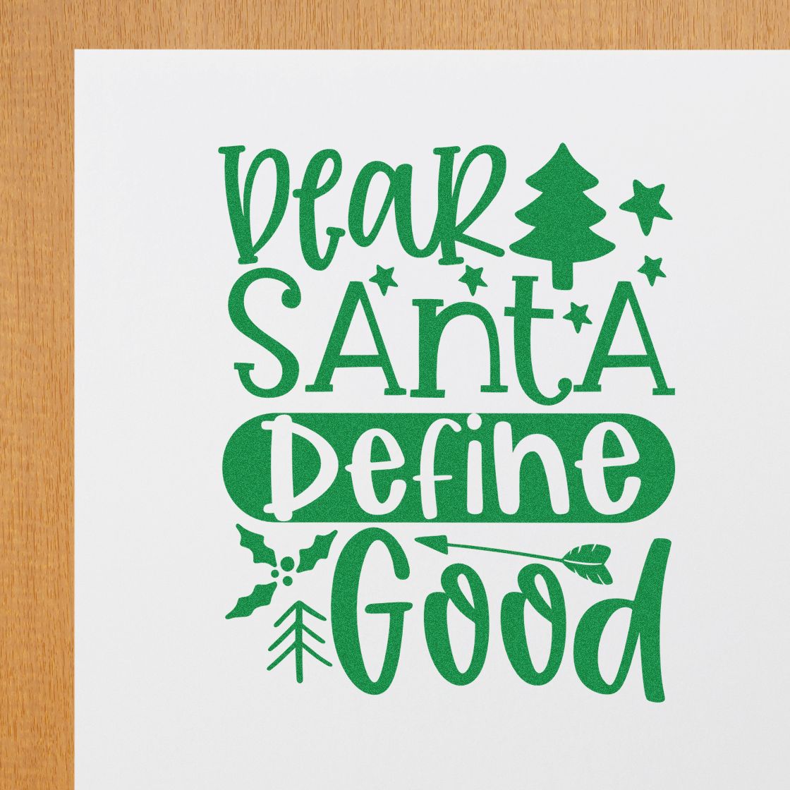 Green holiday stamp design reading Dear Santa Define Good with pine tree, stars, holly and arrow on white paper.