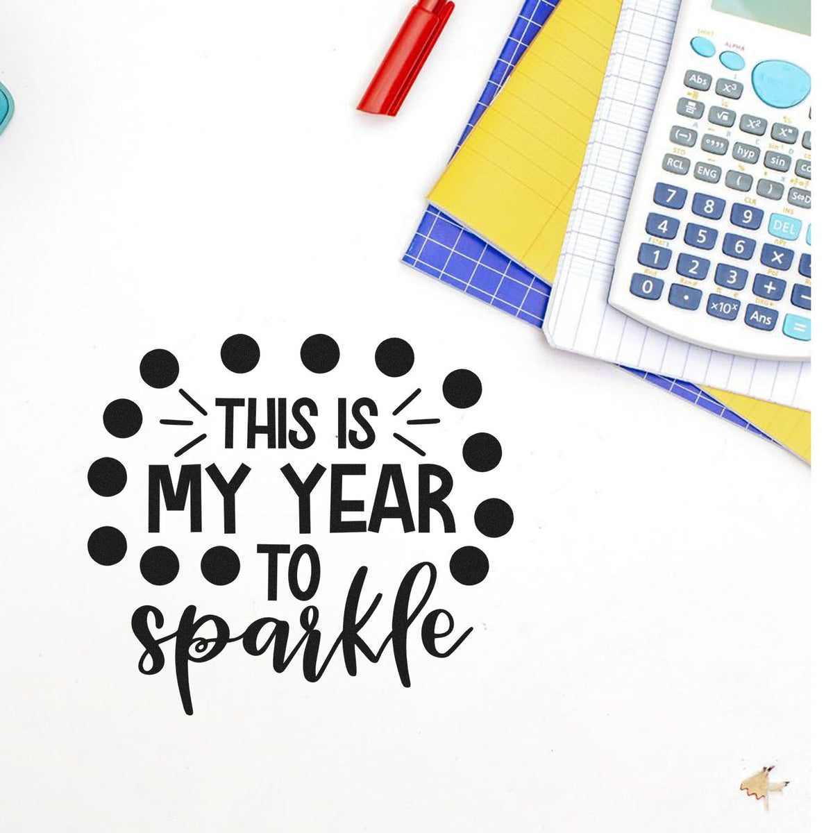 Black This is my year to sparkle stamp and dotted seal, beside colorful notebooks, calculator, and red pen on white.