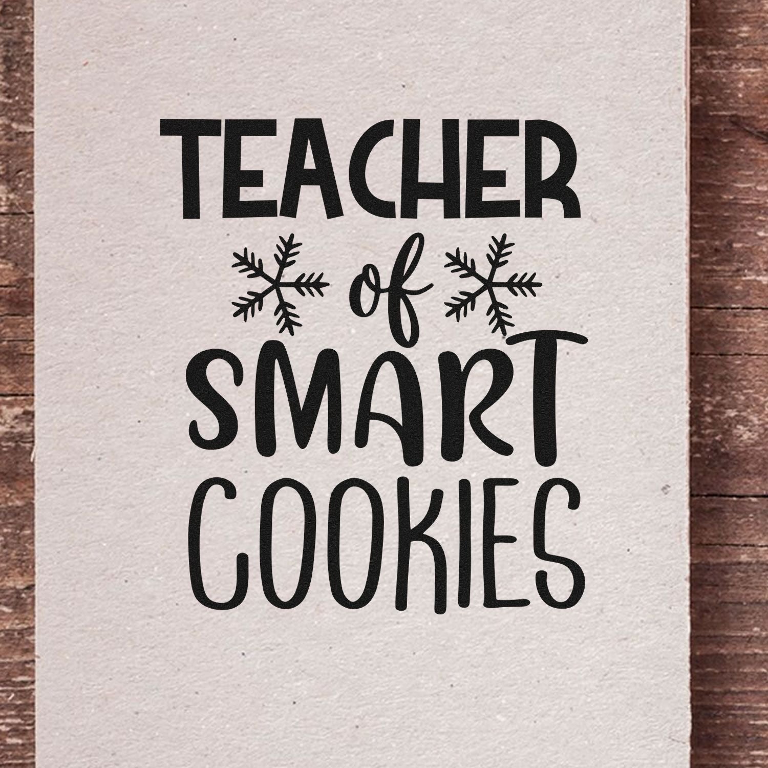 Black teacher rubber stamp design reading Teacher of Smart Cookies with snowflakes on white paper.