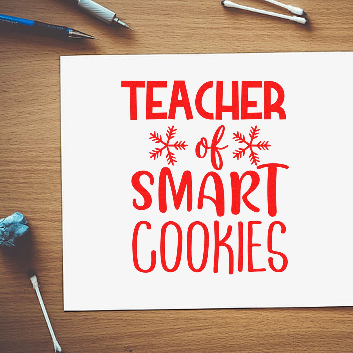 Red teacher stamp and seal design reading Teacher of Smart Cookies on white paper with snowflake accents.