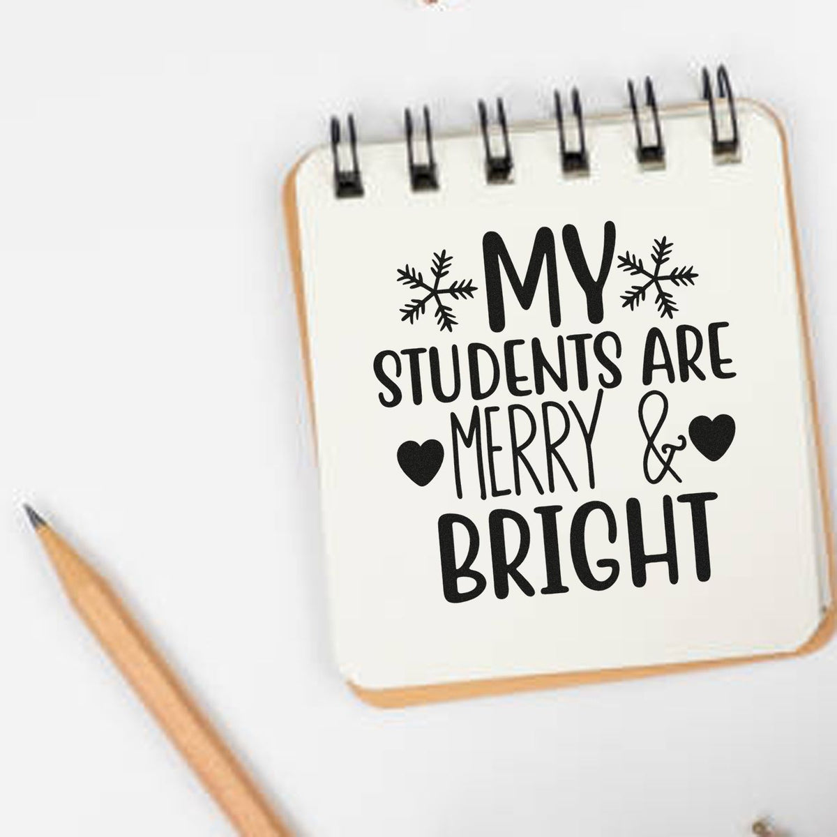 Holiday stamp and seal on cream spiral notebook, black My students are merry & bright text, snowflakes, hearts, and pencil.