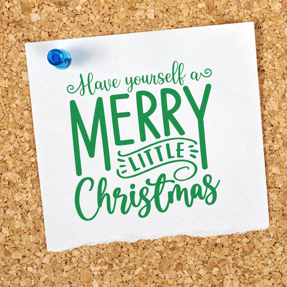 Green Merry Little Christmas stamp seal on white paper, pinned with a blue pushpin against a corkboard background.