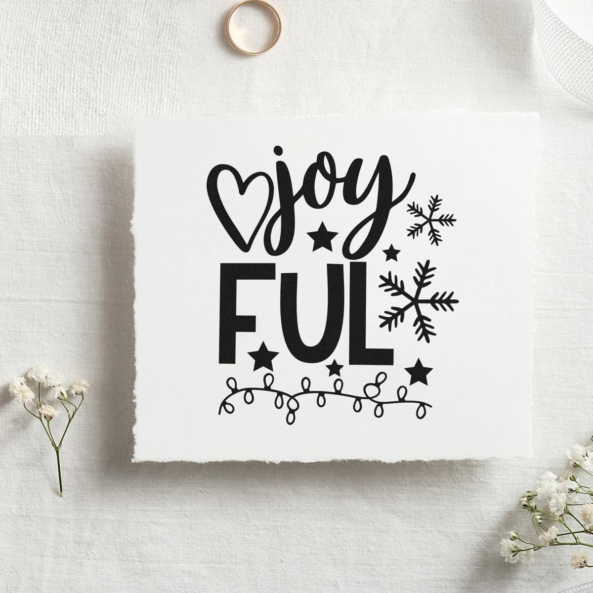 Black holiday stamp seal with joy full, heart, snowflakes, stars, and string lights on white fabric.