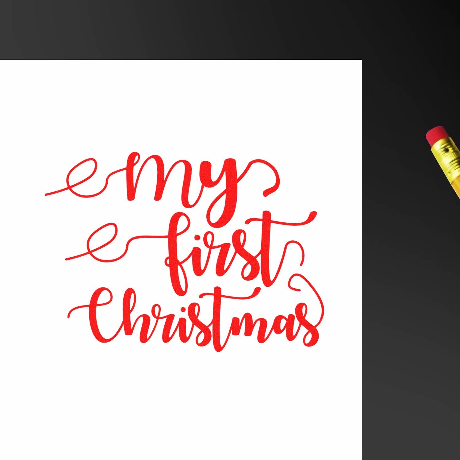 Red my first Christmas stamp/seal design in bright red script on white paper, with a yellow pencil on a dark background.