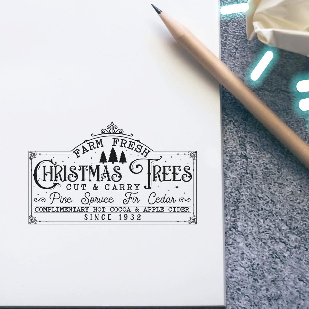 Black decorative Christmas Trees stamp seal on white paper, with pencil on gray textured background