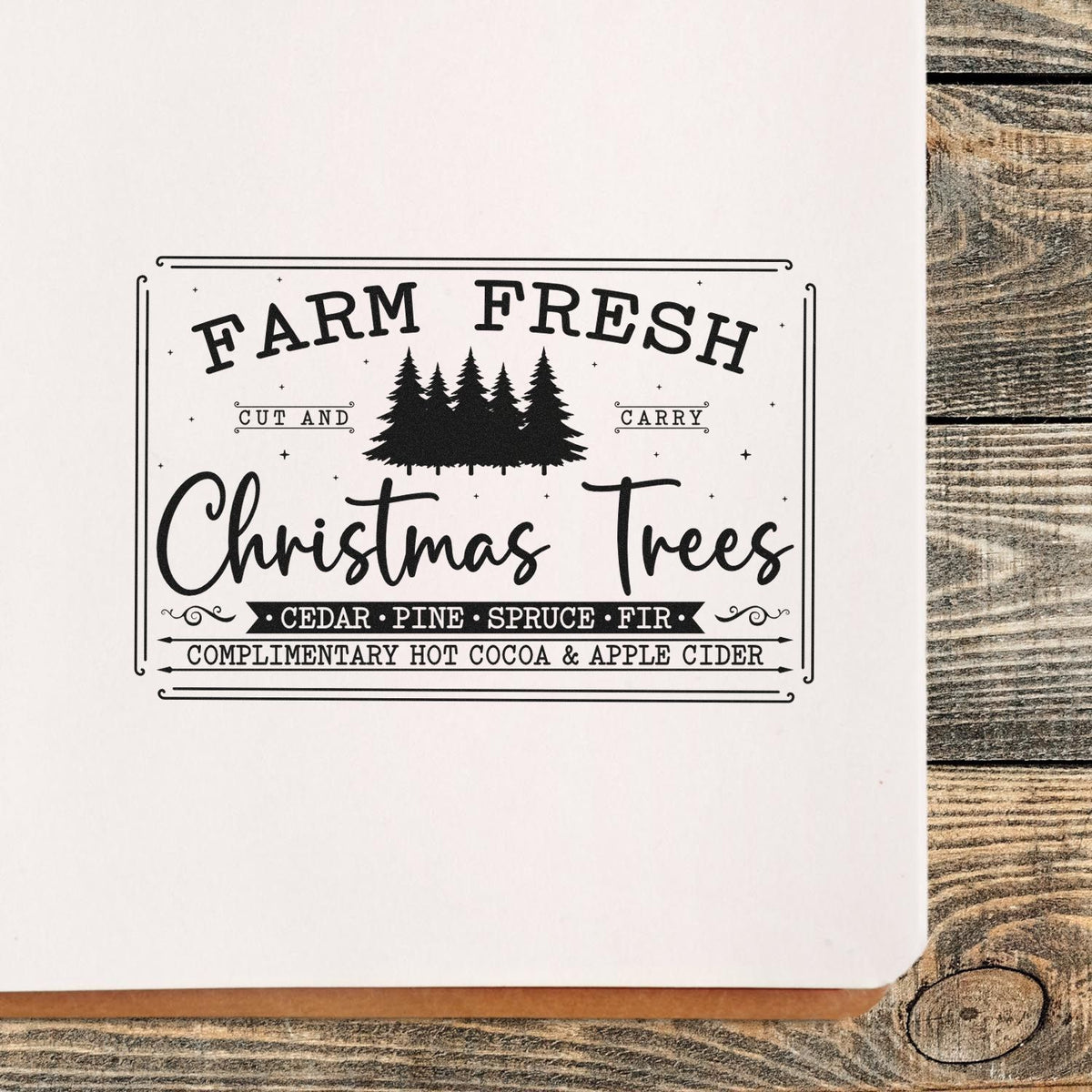 Black Farm Fresh Christmas Trees stamp seal with pine silhouettes on white paper and rustic wood backdrop.