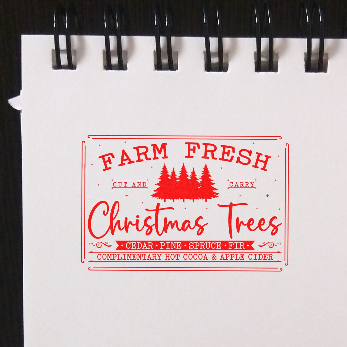Red Christmas tree stamp seal on white paper, with pine silhouettes and text for cedar, pine, spruce, fir, cocoa and cider.