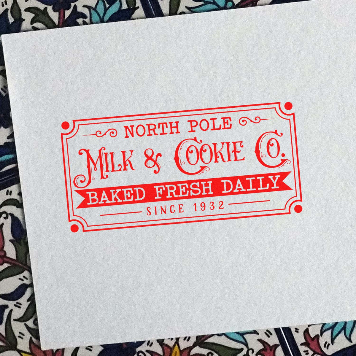 Red decorative stamp seal reading North Pole Milk & Cookie Co. Baked Fresh Daily Since 1932 on white paper.