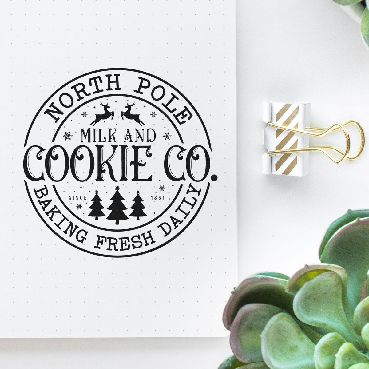 Black North Pole Milk and Cookie Co. stamp seal on dotted notebook page, clipped with gold binder clip.
