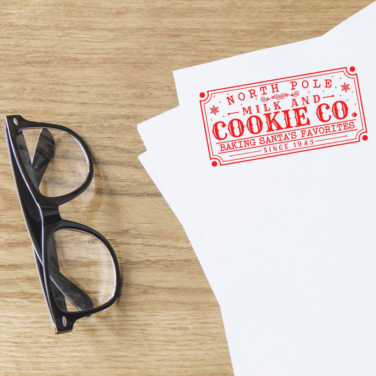 Black eyeglasses beside white papers with a red North Pole Milk and Cookie Co. stamp seal on a wood tabletop.