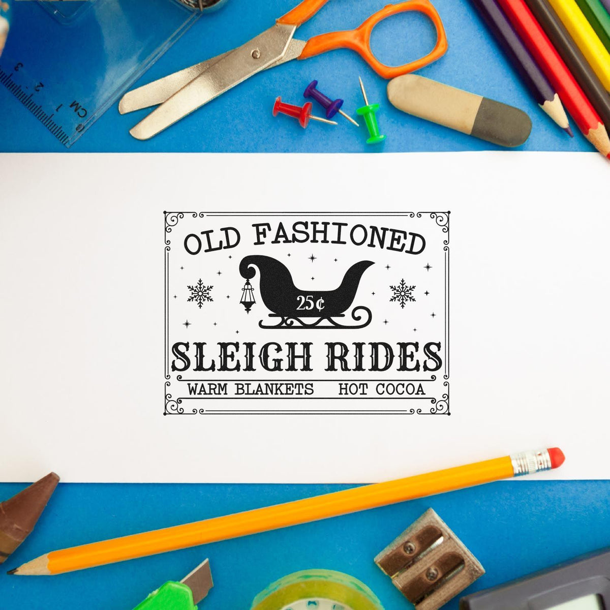 Vintage black stamp seal for Old Fashioned Sleigh Rides on white paper, framed by colorful school supplies on blue.