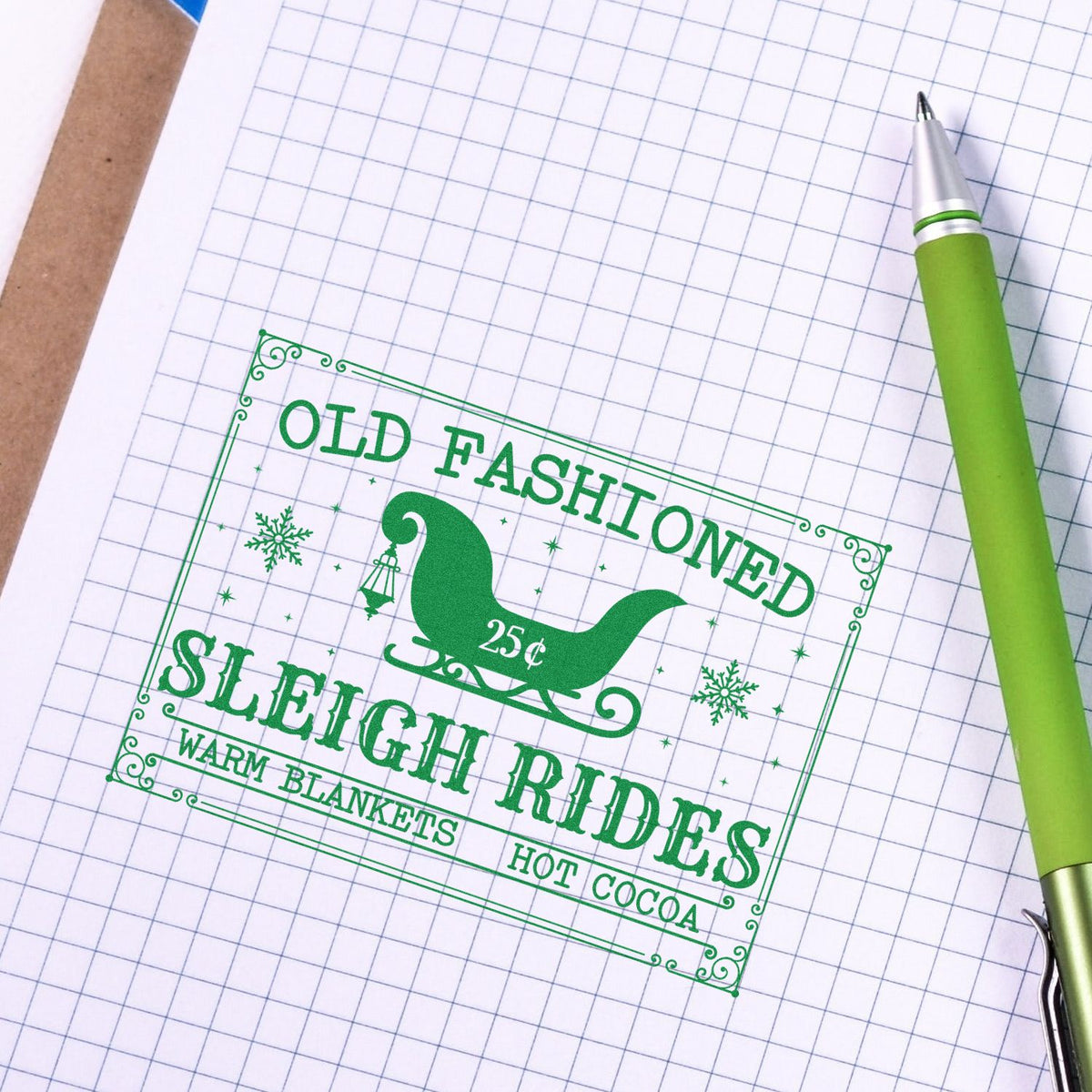 Green vintage sleigh rides stamp seal on graph paper, with a lime-green pen and decorative winter details.