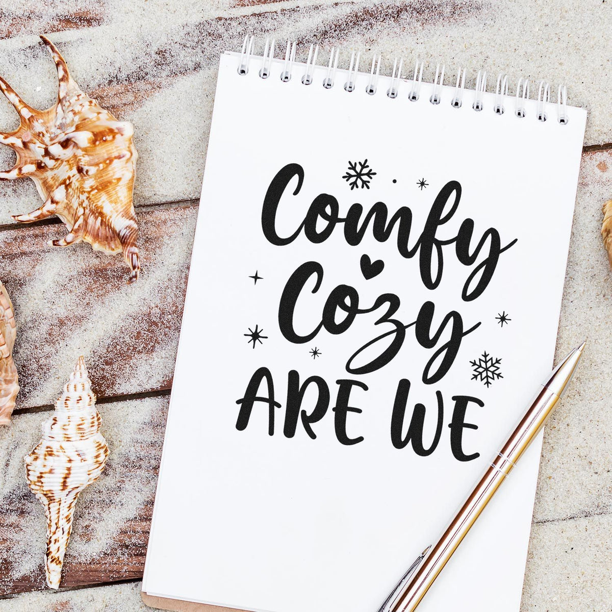 Black Comfy Cozy Are We stamp and seal design on white spiral notebook, with snowflakes, seashells, and gold pen.