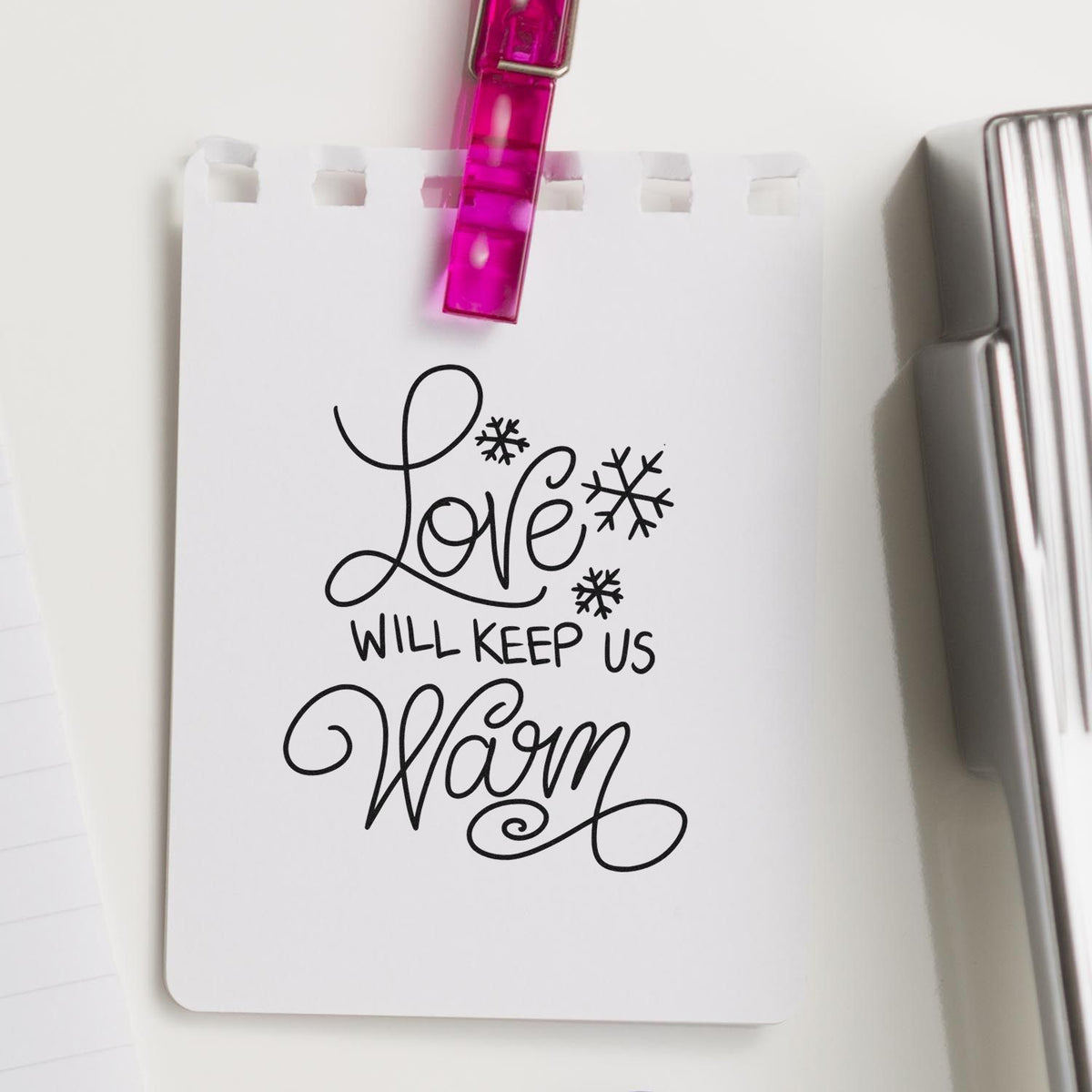 Custom stamp and seal on white card, with black Love will keep us warm script, snowflakes, and pink clip.