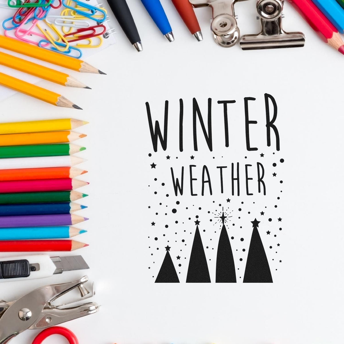 Winter Weather stamp and seal design with black trees and stars, surrounded by colorful pencils, pens, clips, and silver craft tools.