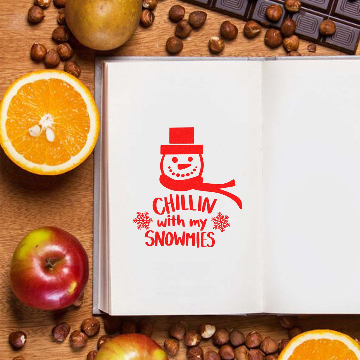 Red holiday stamp seal with snowman and Chillin with my Snowmies on open book, with oranges, apples, and coffee beans.