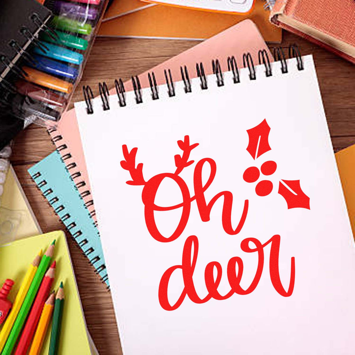 Red holiday stamp and seal on white spiral notebook, surrounded by colorful stationery on a wood desk.