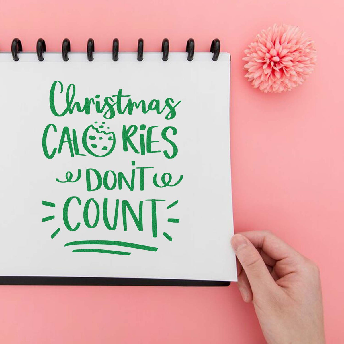 Green Christmas calories dont count stamp/seal on a white spiral notebook, with pink background and pink flower.