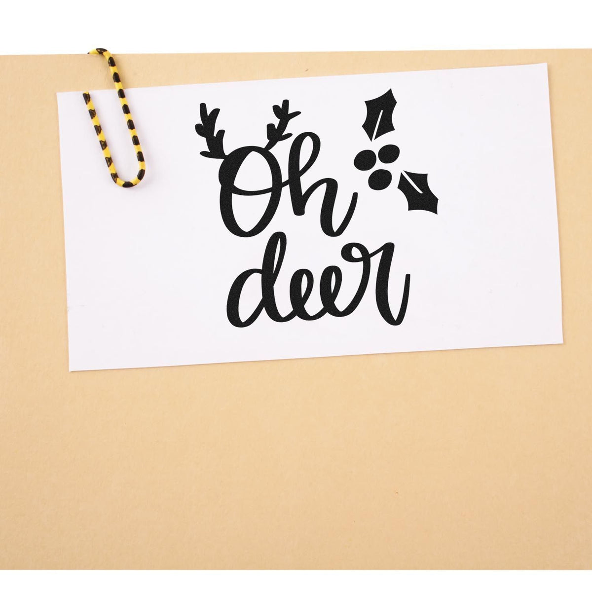 Black Oh deer holiday stamp and seal design on white card, with antlers, holly, and a yellow-striped paperclip.