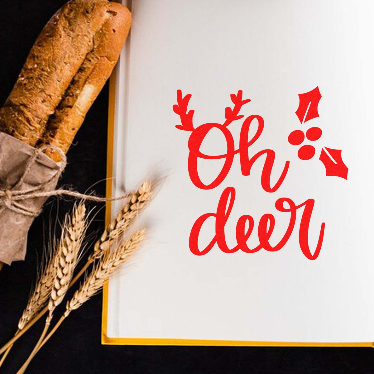 Red Oh deer holiday stamp and seal on a white card with gold trim, beside a rustic bread loaf and wheat stalks.