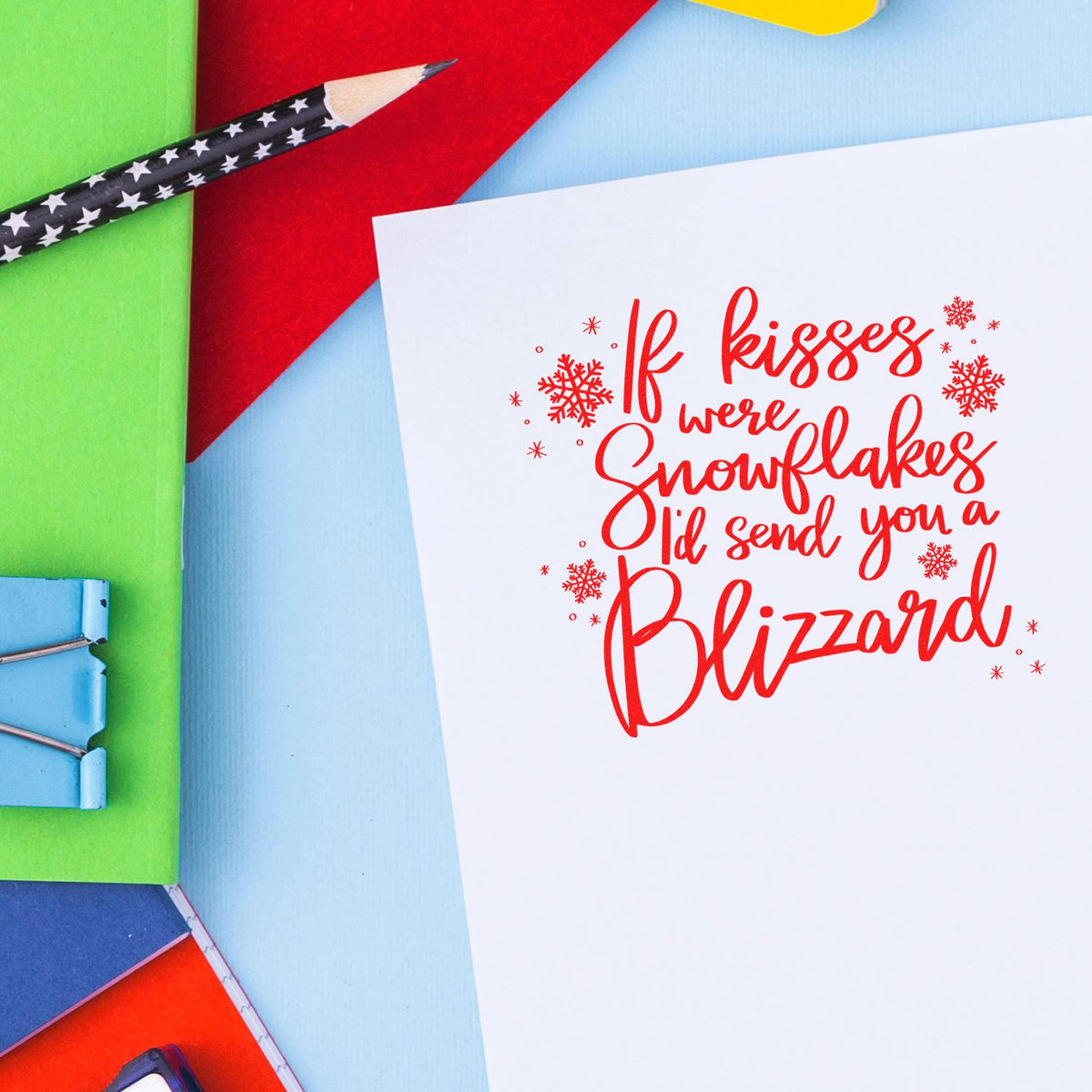 Holiday stamp and seal design with red snowflake lettering on white paper, surrounded by colorful stationery in green, blue, red and yellow.