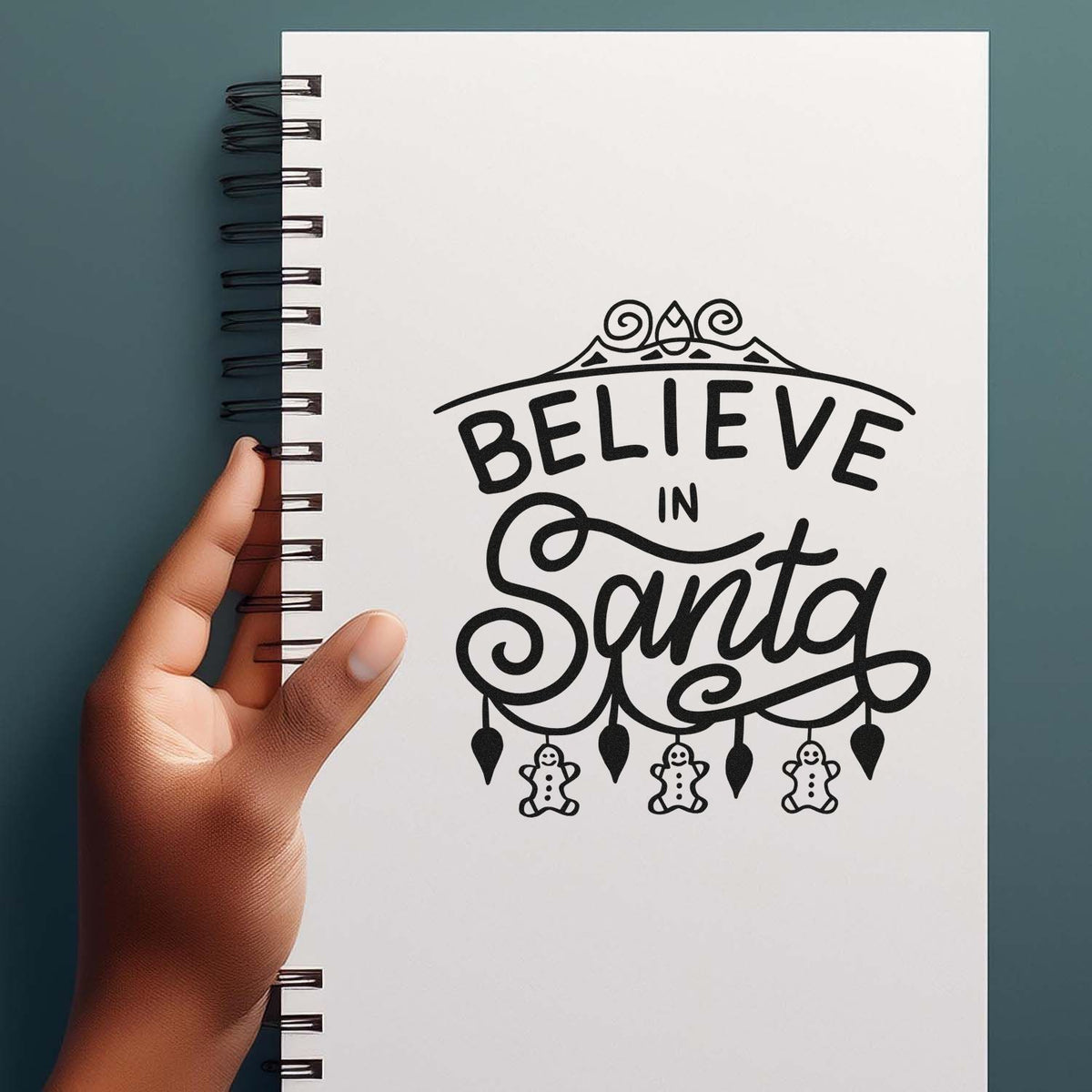 Black Believe in Santa rubber stamp design on a white spiral notebook, with gingerbread accents and decorative swirls.