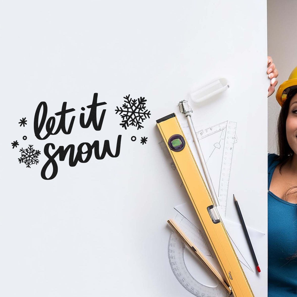 Custom stamp and seal products on white board with black let it snow text, snowflakes, yellow seal tool, rulers, and pencil.