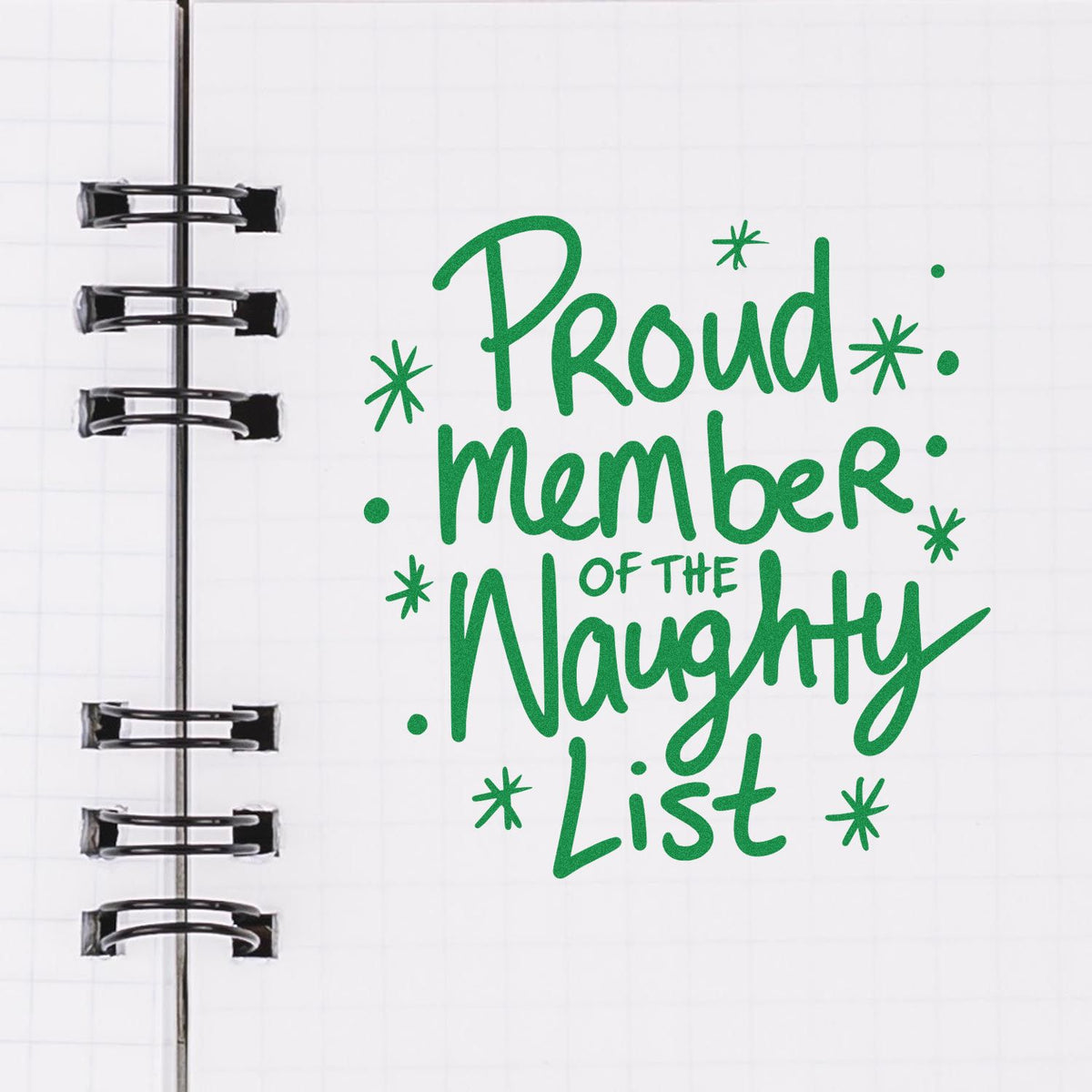 Green script stamp reading Proud Member of the Naughty List on a white notebook page with black binder rings.