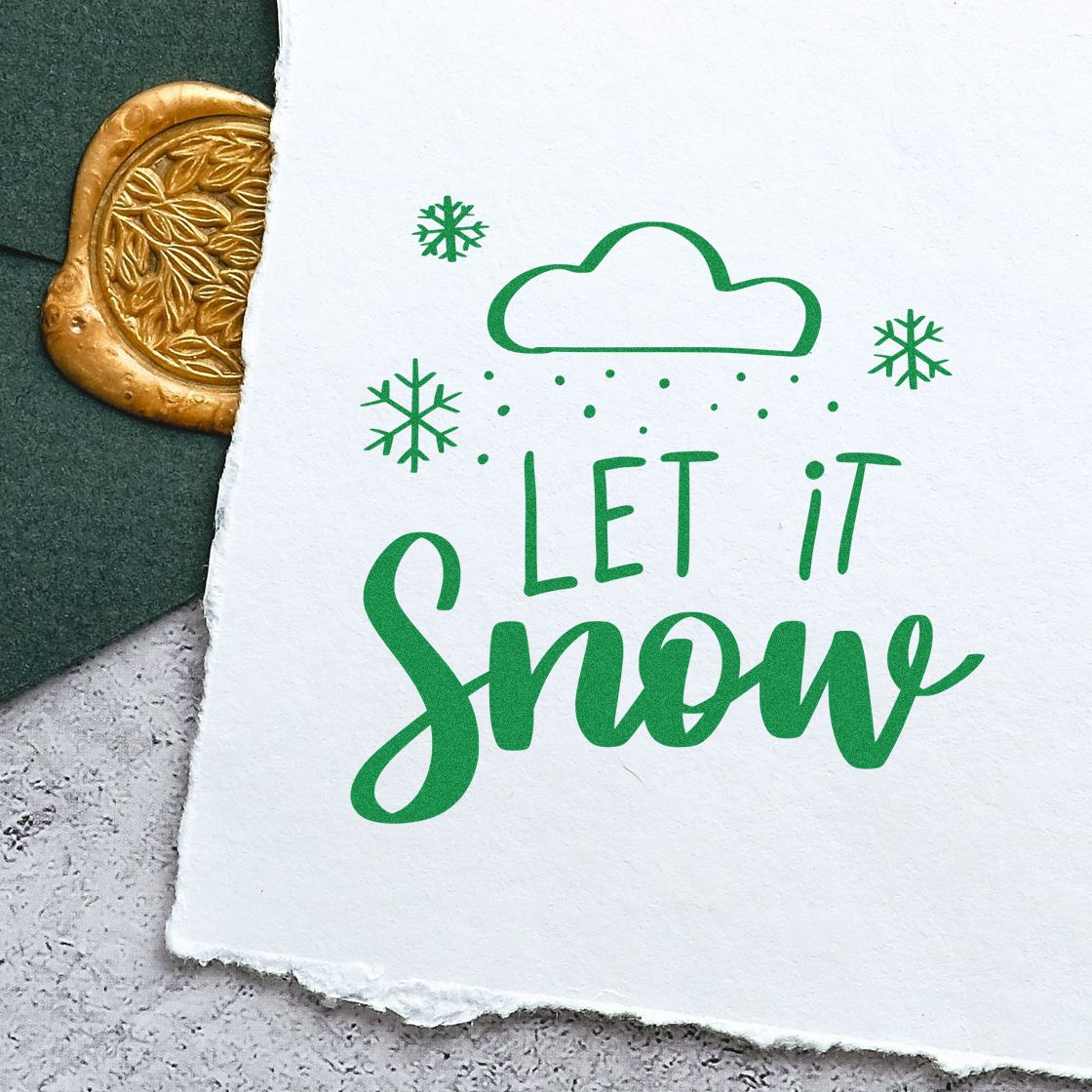 Green Let it Snow holiday stamp with cloud and snowflakes on white paper, beside a gold embossed wax seal.
