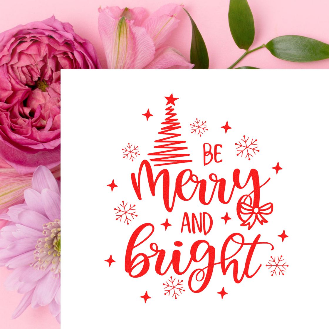 Red holiday stamp and seal reading Be Merry and Bright with tree, snowflakes and bow on a white card over pink flowers.