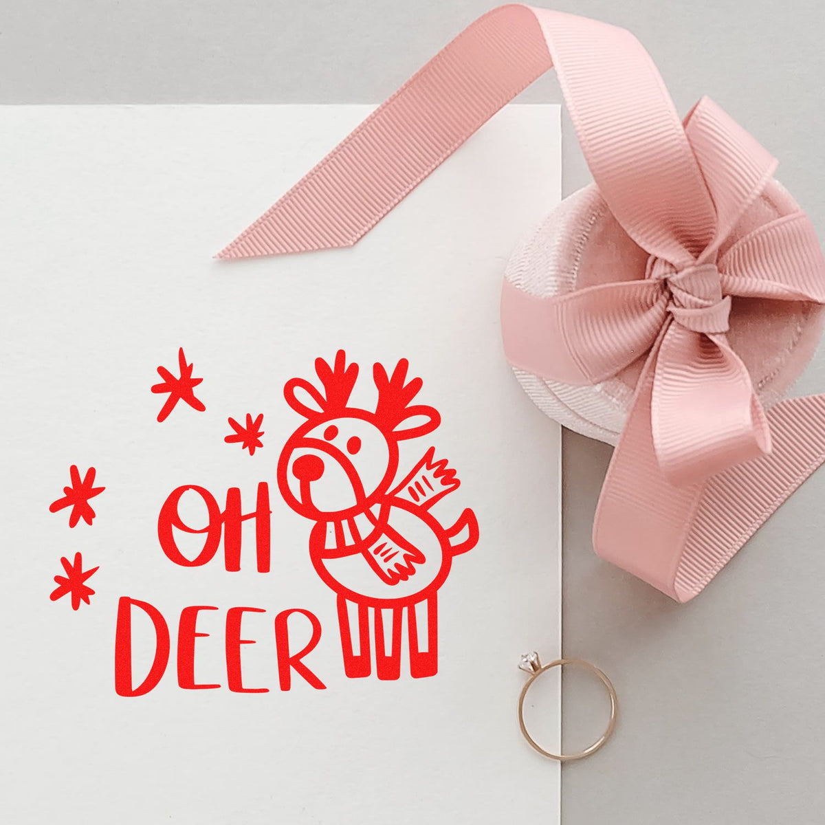 Red OH DEER stamp on white paper with a pink ribbon bow seal and ring, featuring a festive deer design.