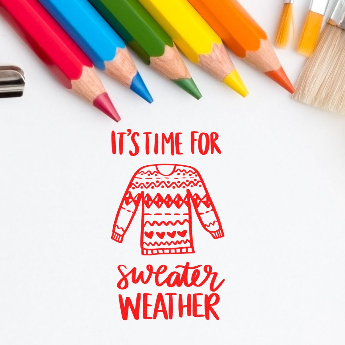 Red sweater-weather stamp/seal with sweater icon and handwritten text, framed by colorful pencils on a white background.