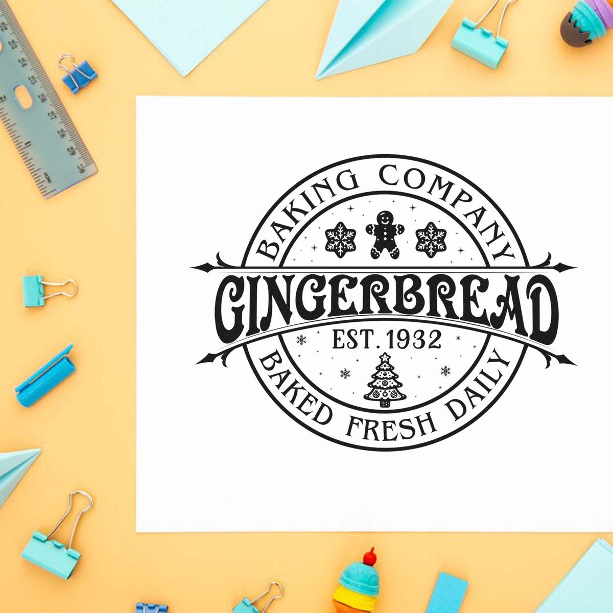 Black gingerbread bakery stamp seal on white paper, framed by blue office supplies on a yellow background.