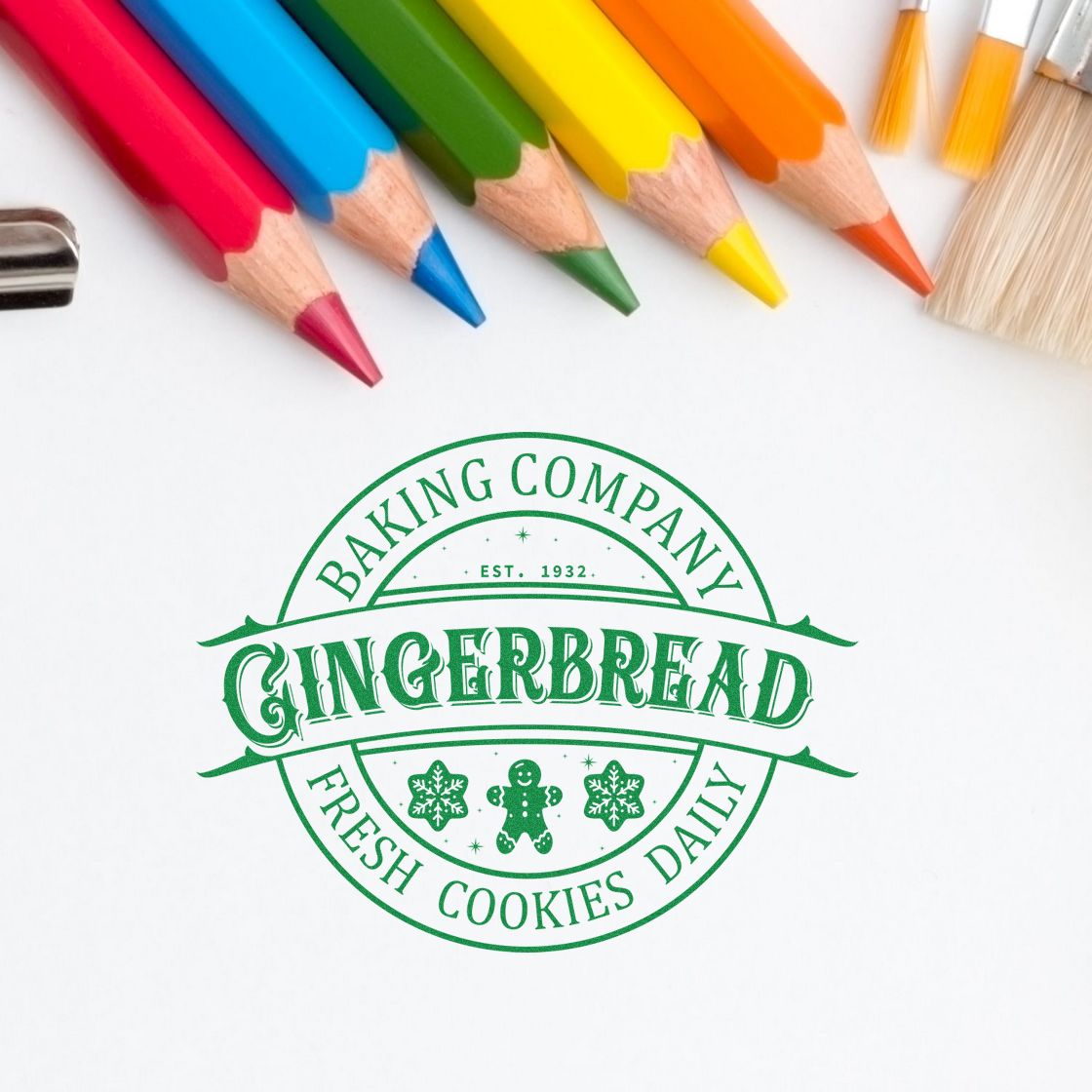 Green gingerbread bakery stamp seal on white paper, framed by red, blue, green, yellow and orange pencils.