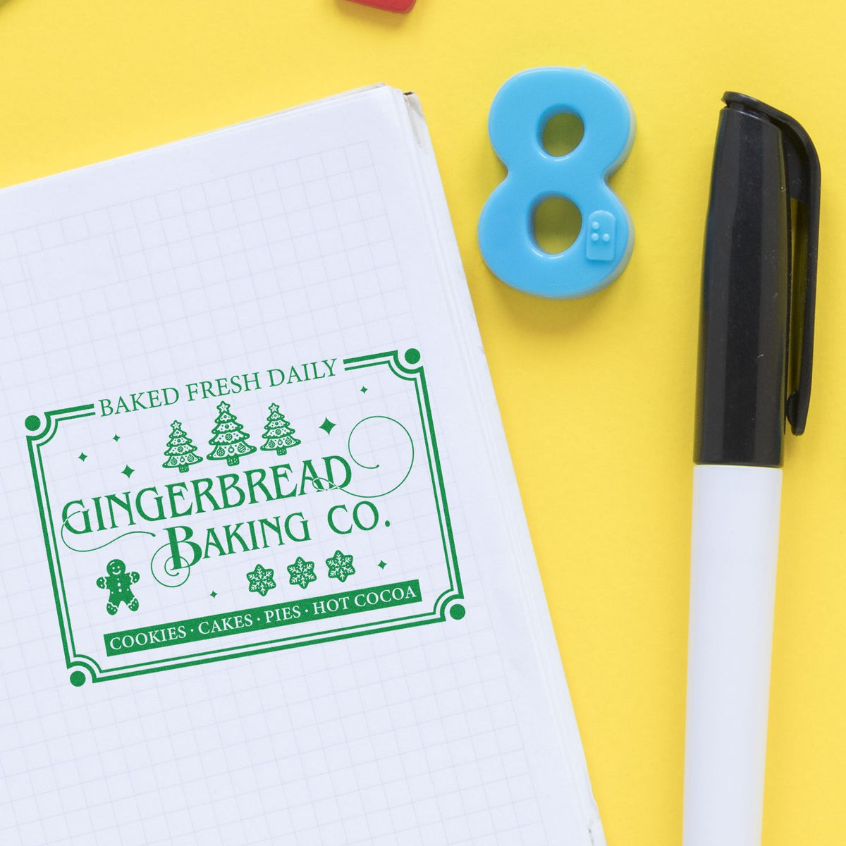 Green Gingerbread Baking Co. bakery stamp on notebook, with blue number 8 seal and black pen on yellow background
