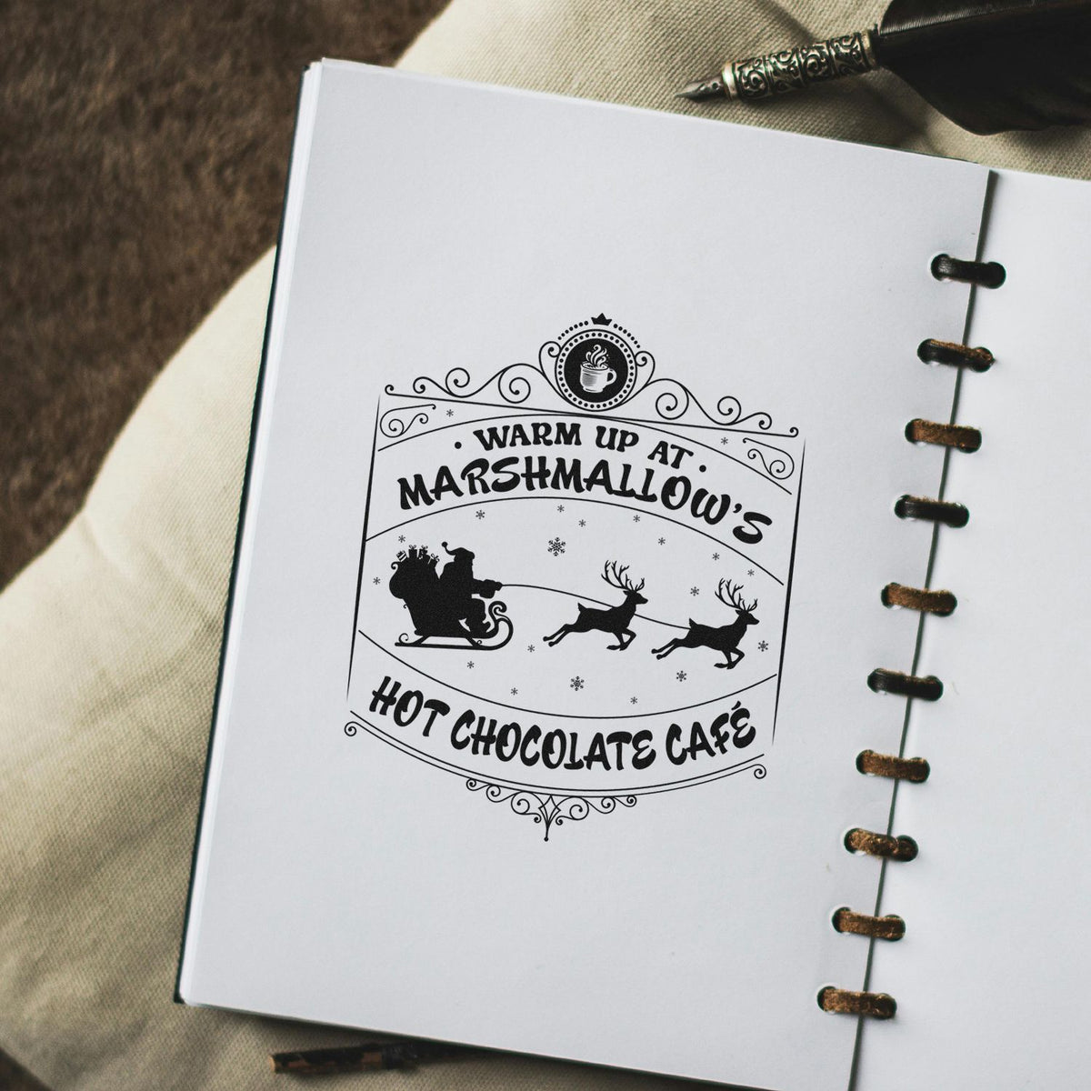 Black decorative stamp seal for Warm Up at Marshmallows Hot Chocolate Cafe with Santa sleigh, reindeer, and coffee cup on white paper.