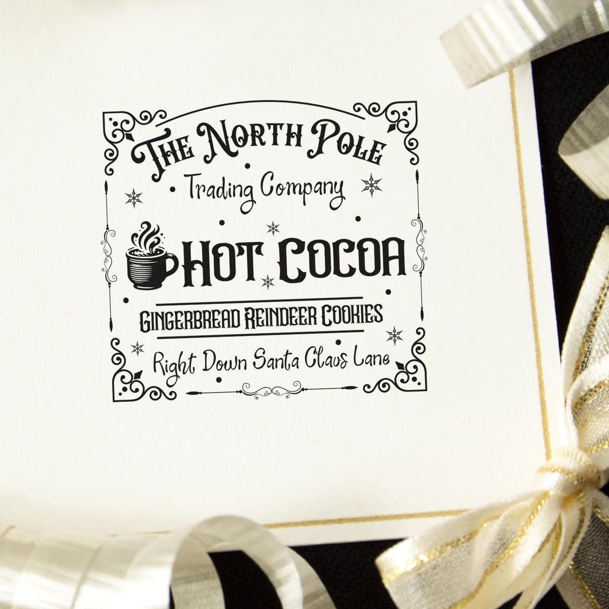 Custom black holiday stamp seal reading Hot Cocoa with ornate border, on cream paper with gold ribbon.