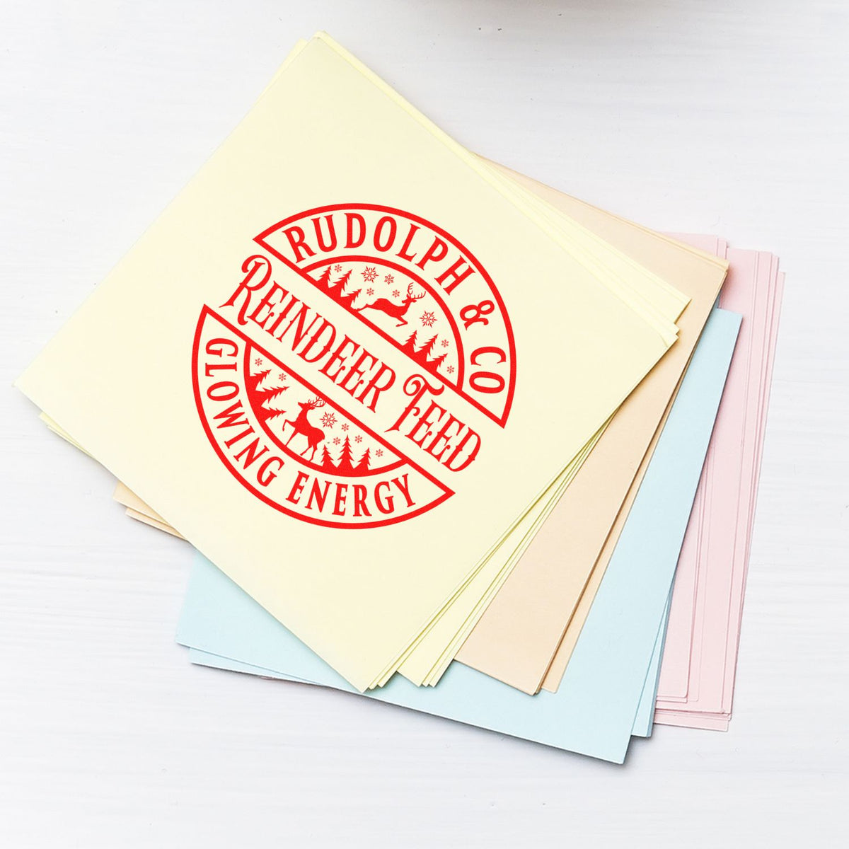 Stack of pastel stamp and seal papers with a red Rudolph & Co Reindeer Feed Glowing Energy holiday seal.