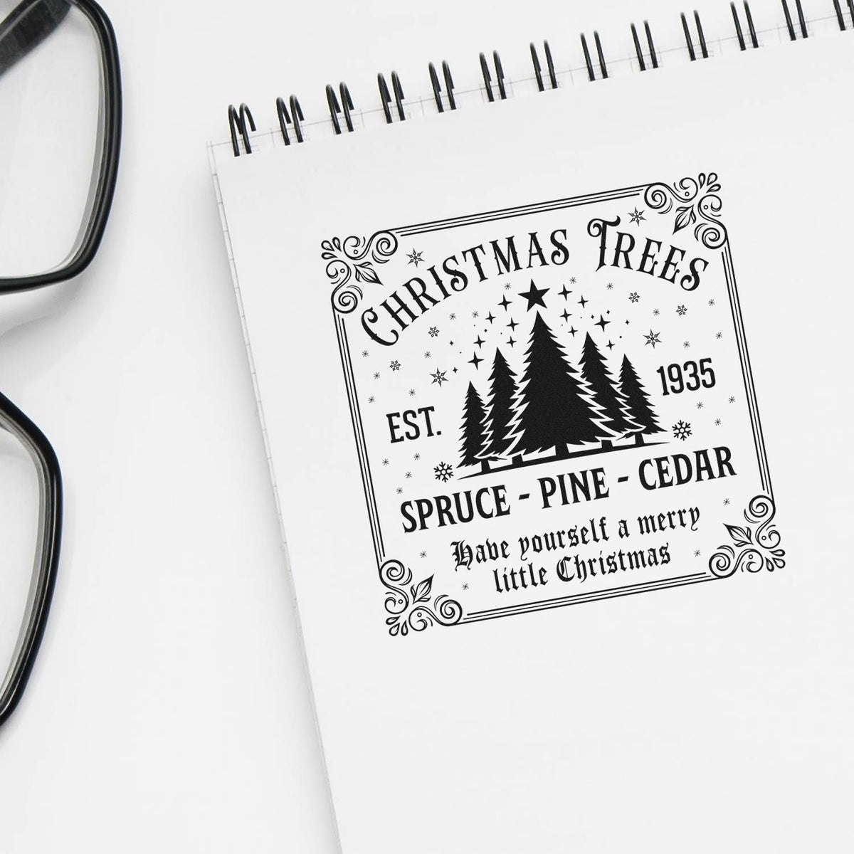 Black Christmas Trees stamp seal design on white notebook, with pine silhouettes, stars, and vintage Christmas lettering.