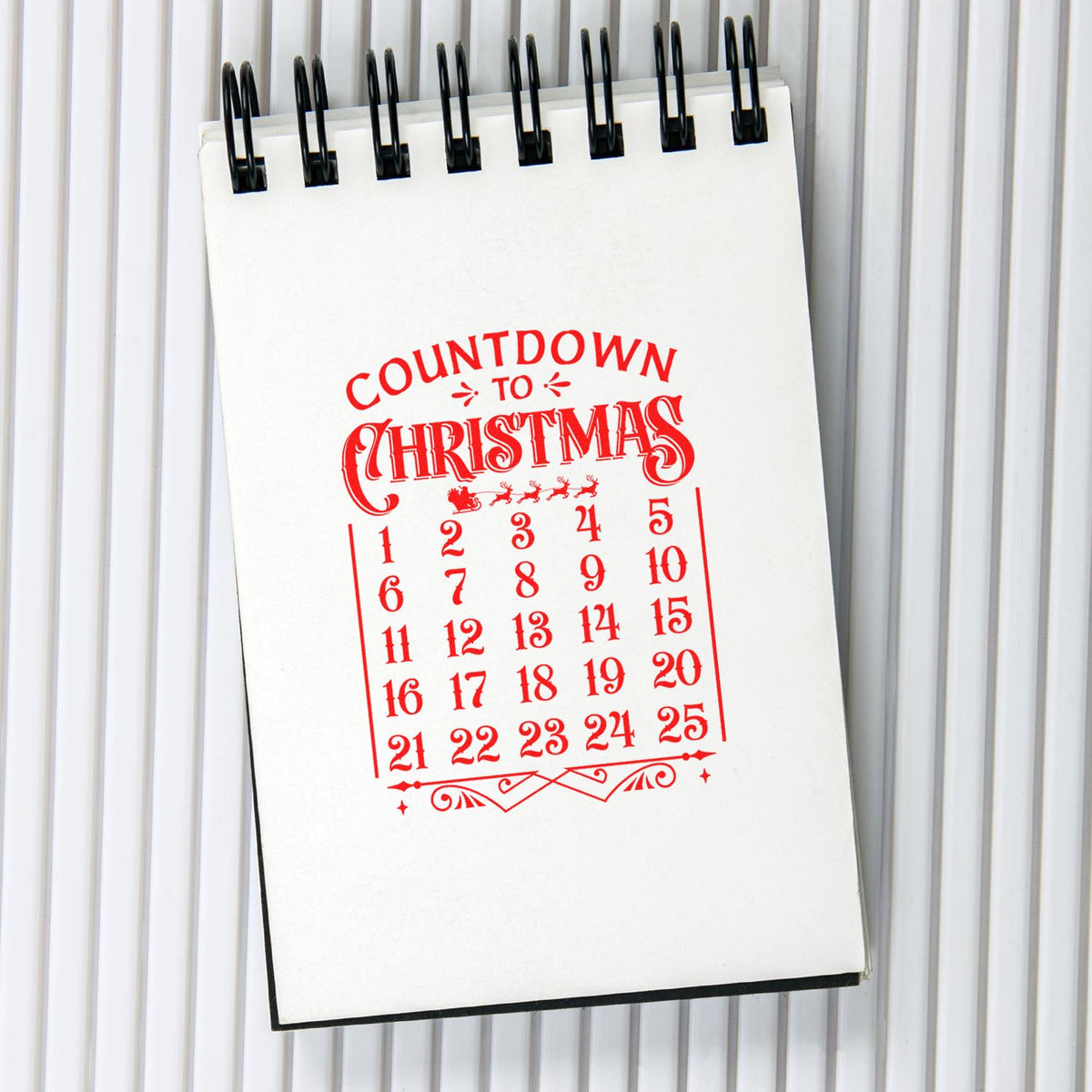 Christmas countdown stamp and seal on white spiral notepad, red calendar design, gray ribbed background.