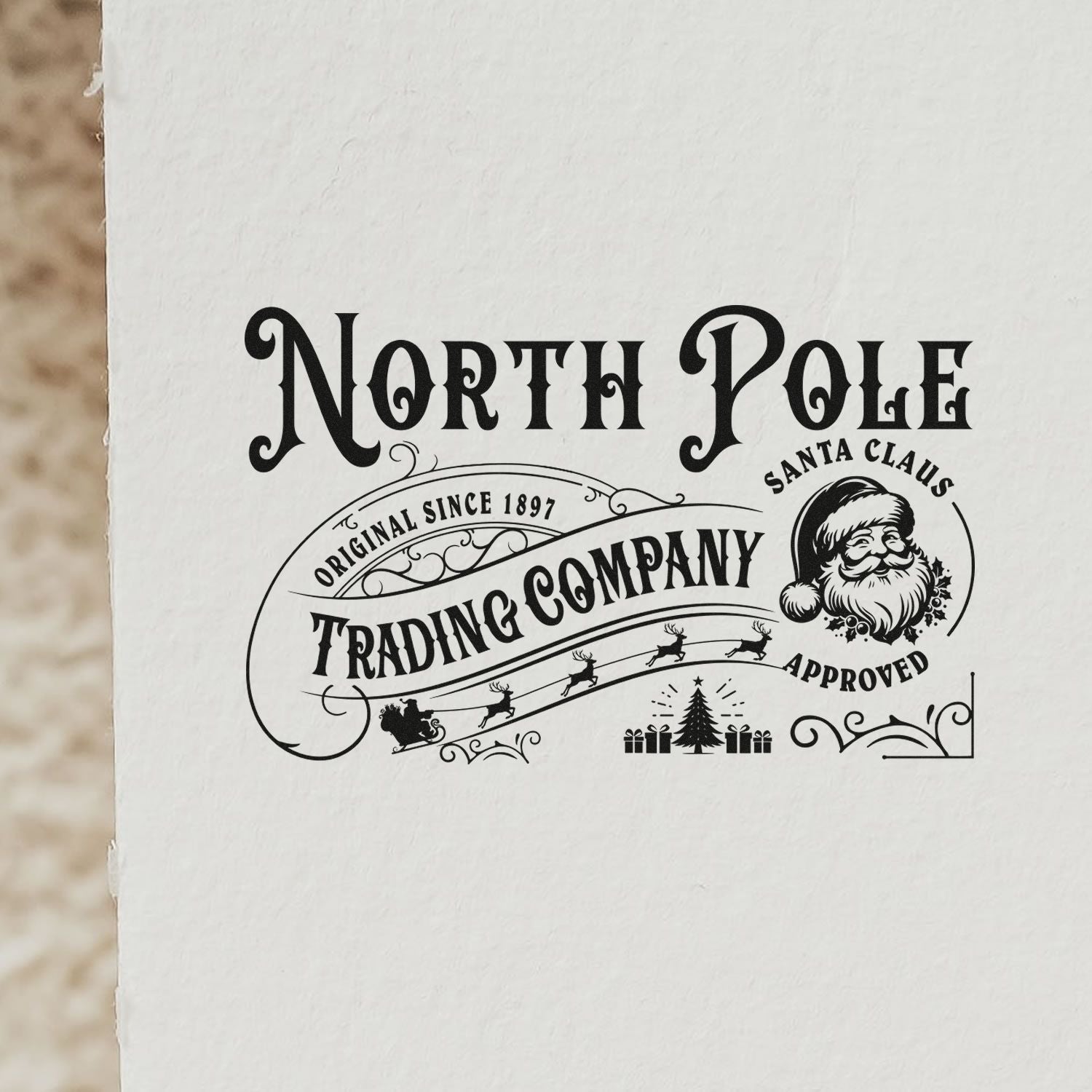 Black vintage North Pole Trading Company stamp seal on white paper, with Santa, sleigh, gifts, tree, and Approved text.